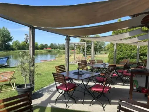 Sessel und Sonnenschutz mit Tischen und See mit Liegewiese im Hintergrund